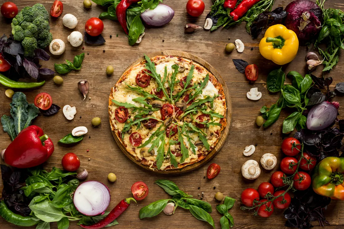 Pizza surrounded by fresh vegetables and herbs